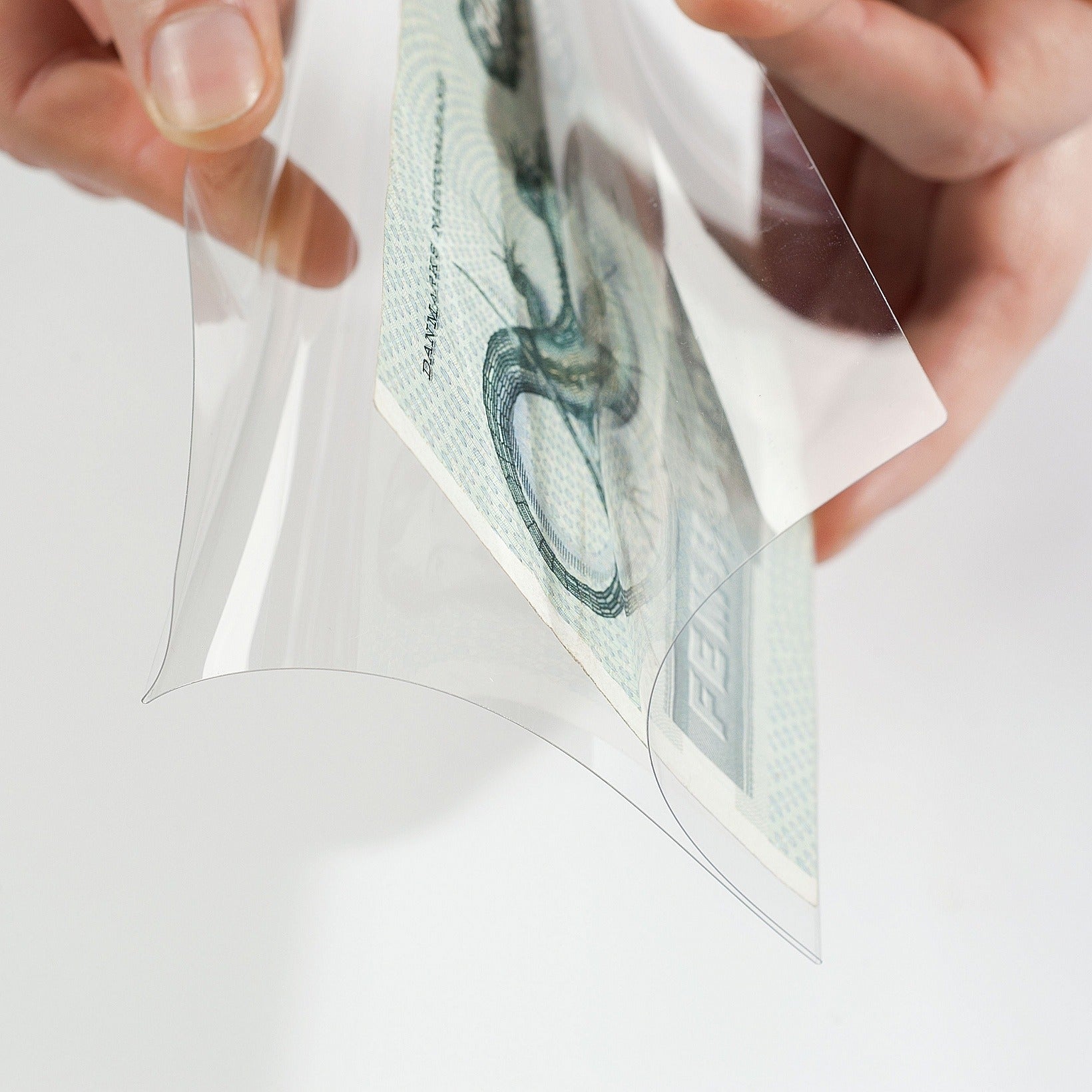 Person holding a banknote inside a clear protective sleeve on a white background
