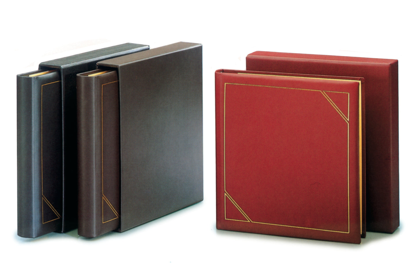 Collection of leather-bound albums in black, red and brown colors with gold accents alongside the matching slipcases on a white backgrounding