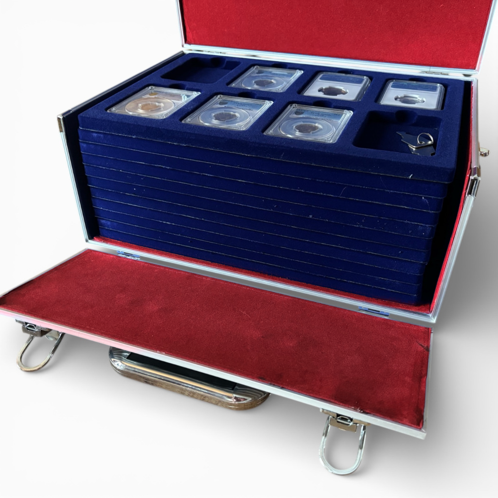 Aluminum coin case with a red interior & blue trays filled with graded coin slabs in the tray compartments on a white background