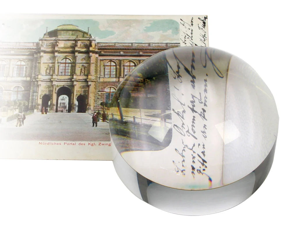 Solid glass dome magnifier with a postcard with a picture of a building and script on a white background