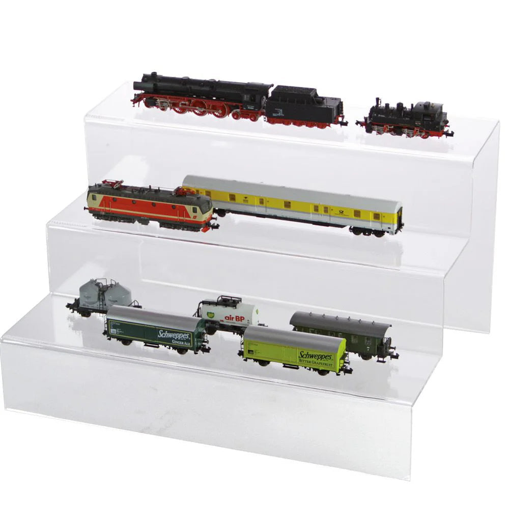 Clear acrylic display steps with various toy model trains on a white background