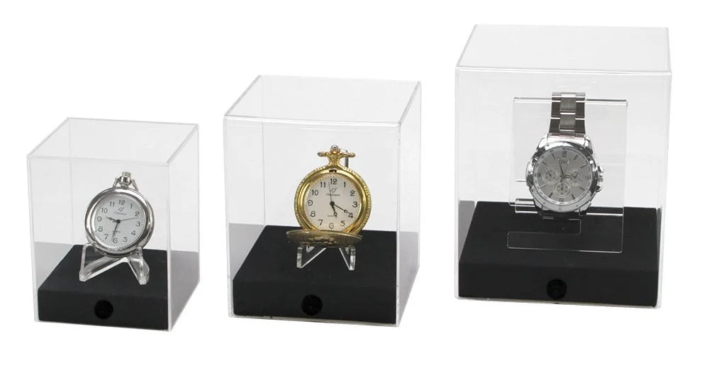 Three watches on acrylic easels/stands in acrylic display cube cases with black bases on a white background