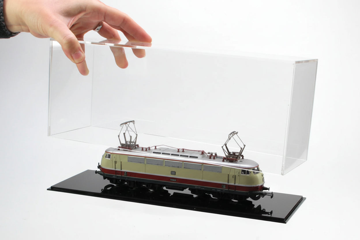 Model train in a clear acrylic display case with a hand lifting off the lid with black bottom on a white background