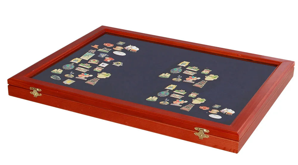 Wooden display case with a closed glass lid displaying various collectible pins on a blue velvet insert on a white background.