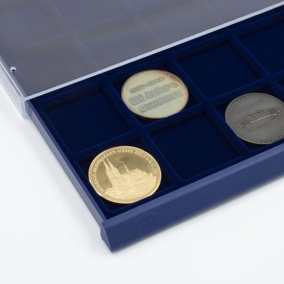 Detail shot of open acrylic stackable drawer unit with a blue velvet tray and square compartments holding coins on a white background