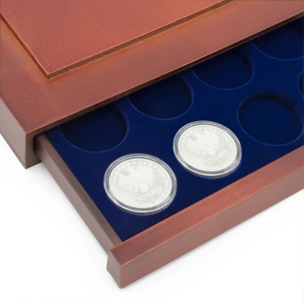 Detail shot of open wooden stackable drawer unit with a blue velvet tray with circular compartments holding coins on a white background
