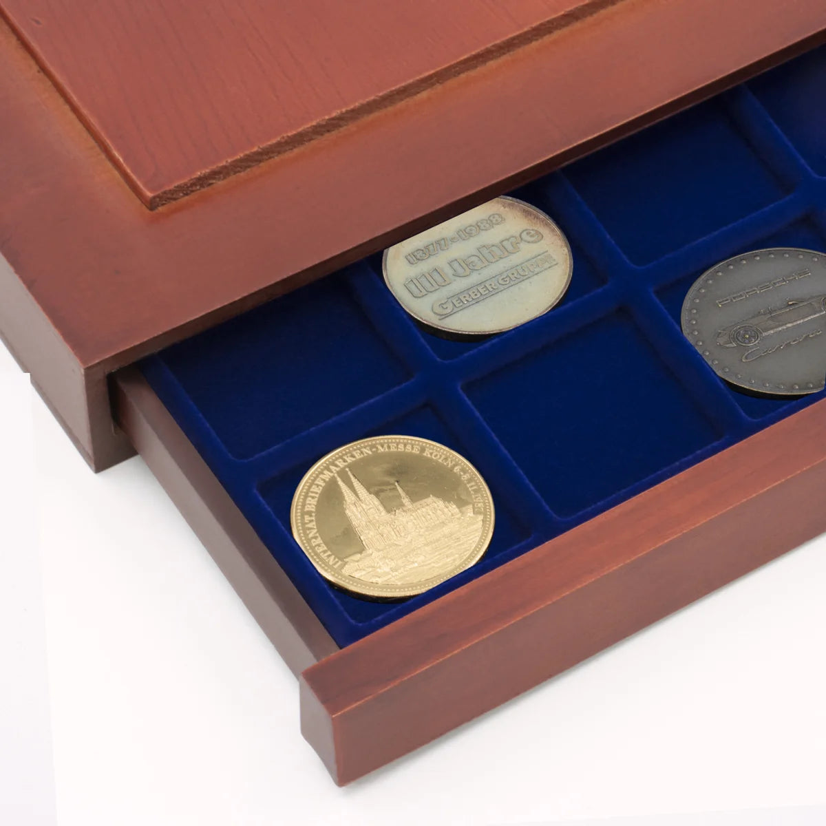 Detail shot of open wooden stackable drawer unit with a blue velvet tray with square compartments holding coins on a white background