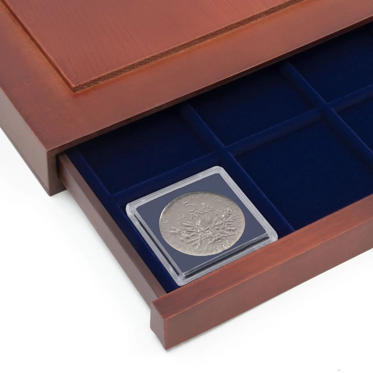 Detail shot of open wooden stackable drawer unit with a blue velvet tray with a plastic 2x2 coin flip on a white background