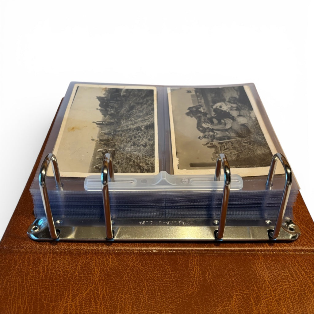 Detail image of the ring mechanism of a tan stamp album laid open with transparent pages displaying black and white photos on a white background