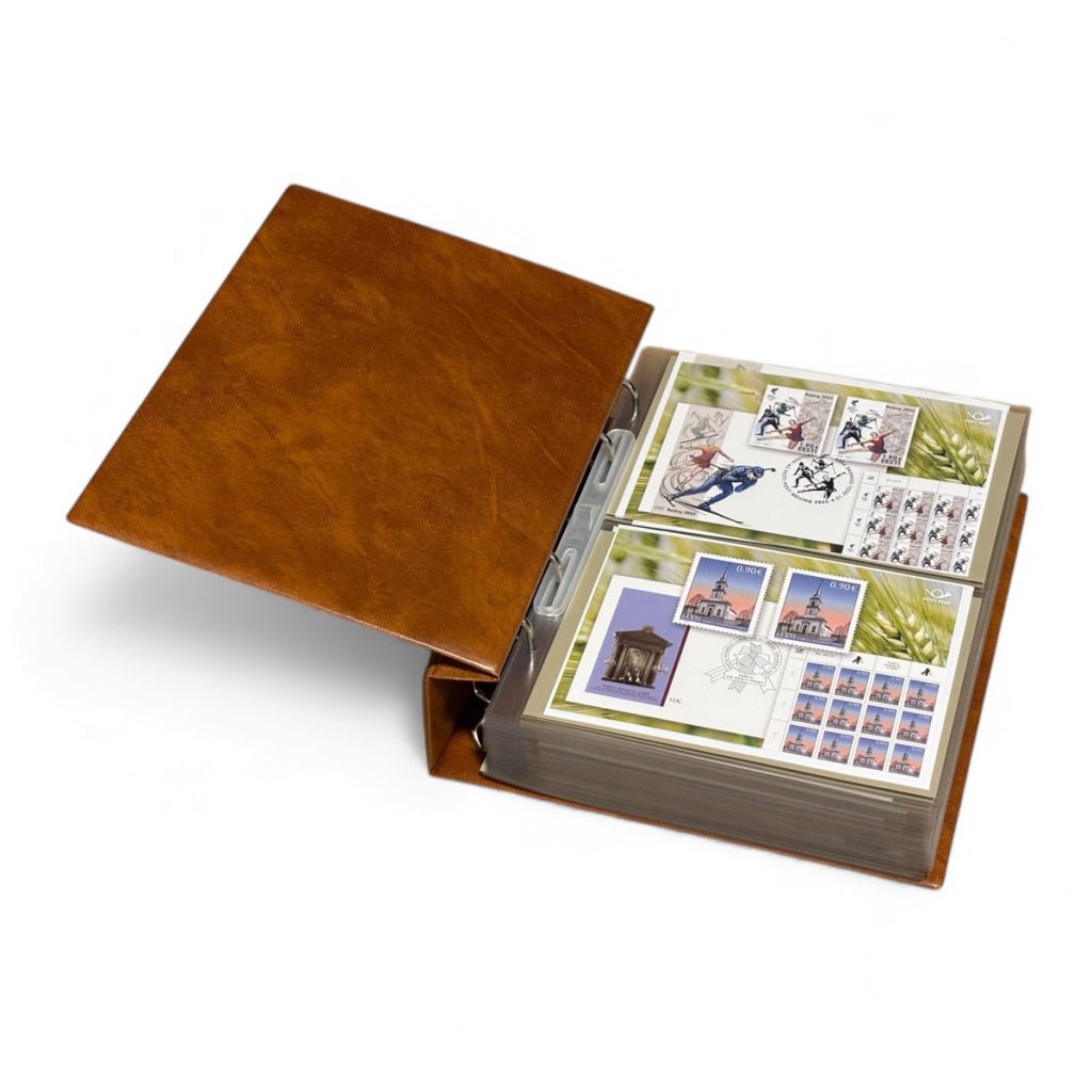 Tan stamp album laid open with transparent pages displaying stamps & covers on a white background