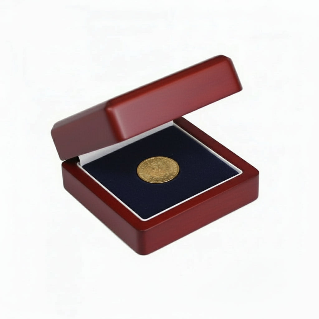 Gold coin in a wooden box laying on the blue velvet impressionable foam with cream lining on a white background