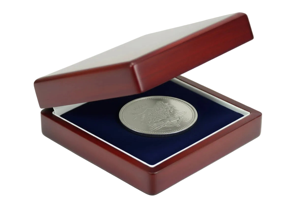 Silver coin in a wooden box laying on the blue velvet impressionable foam with cream lining on a white background