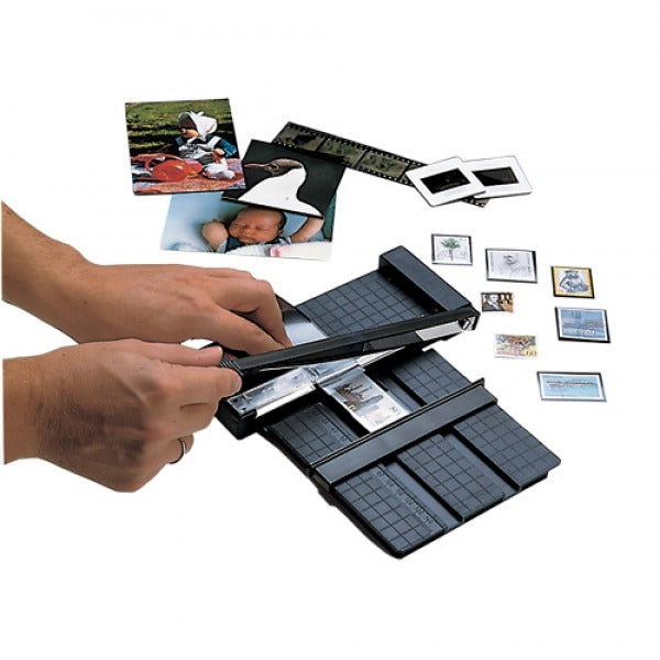 Small black stamp mount cutter being used and surrounded by other stamps and photos on a white background