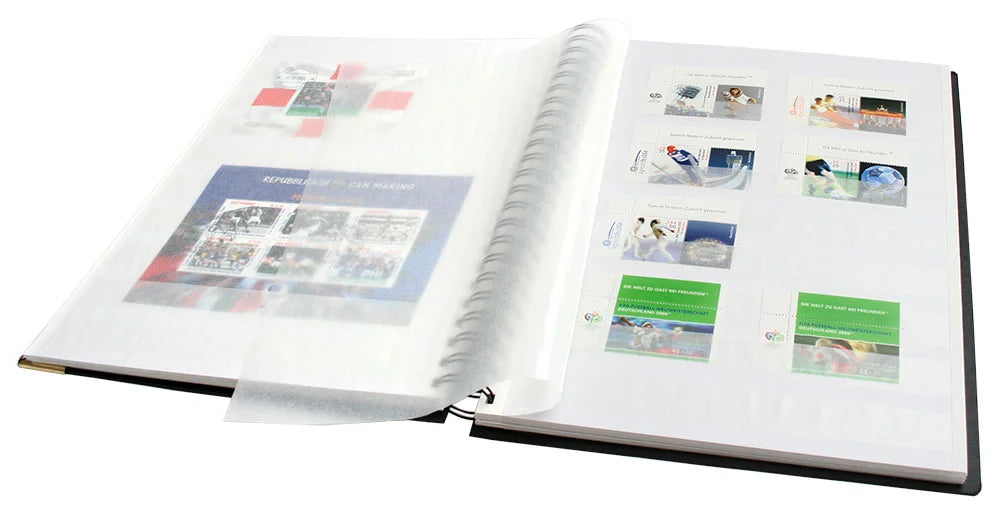 Designer spiral-bound black stamp stockbook with 32 white pages, glassine interleaves, and gold embossed Post Horn, laid open displaying stamps inside the parchment strips, on a white background