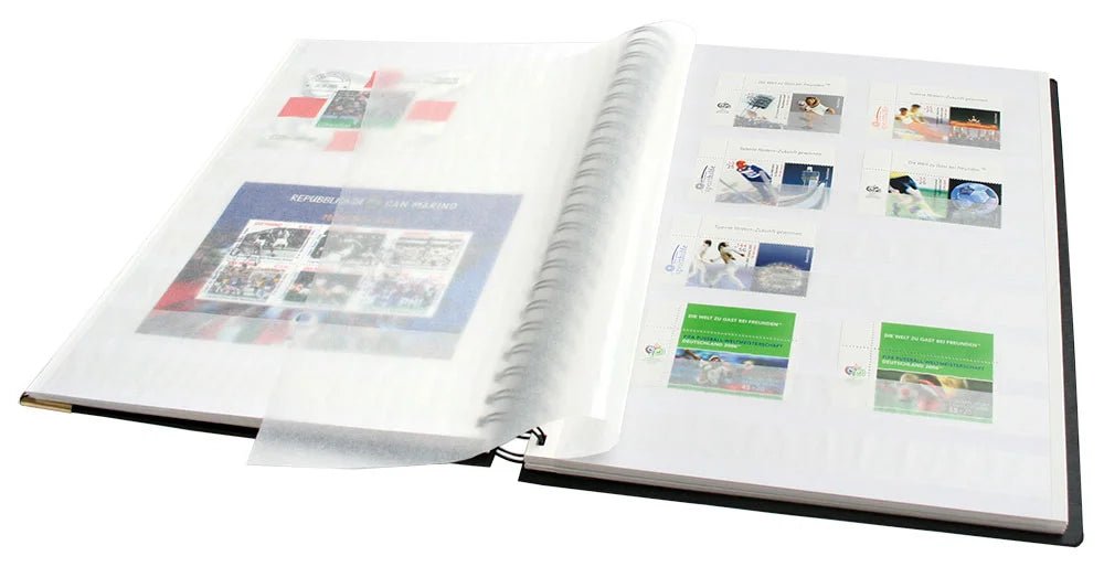 Designer spiral-bound black stamp stockbook with 32 white pages, glassine interleaves, and gold embossed Post Horn, laid open displaying stamps inside the parchment strips, on a white background