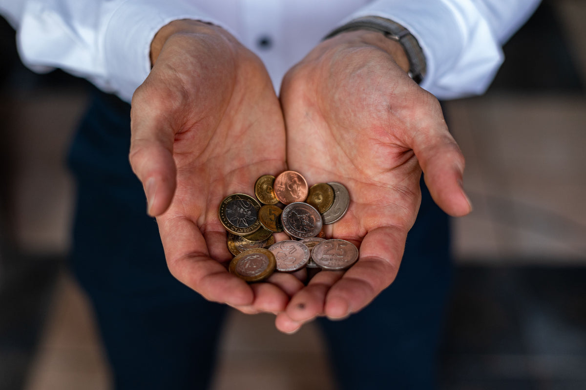 A close-up of a person's cupped hands holding a small pile of assorted coins, with a white shirt and dark pants visible in the background.