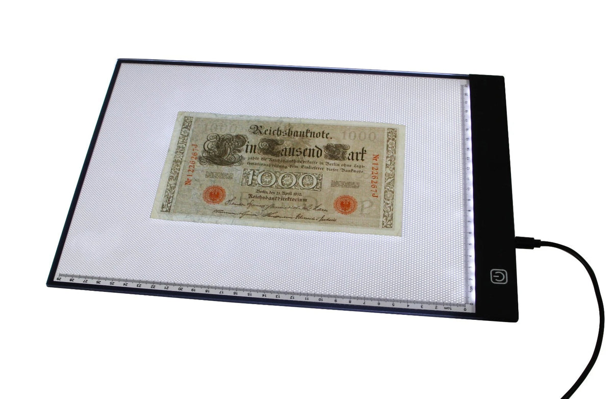 A rectangular light box document illuminator with a black frame and a built-in ruler, showing a vintage German 1000 Reichsmark banknote under bright white light. A power cord extends from the right side of the device against a solid white background.
