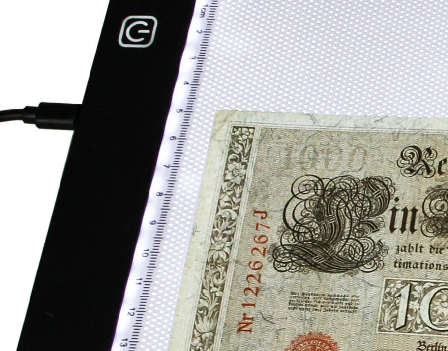 A close-up of a light box with a ruler scale on the side, illuminating a vintage-style banknote on a white background.