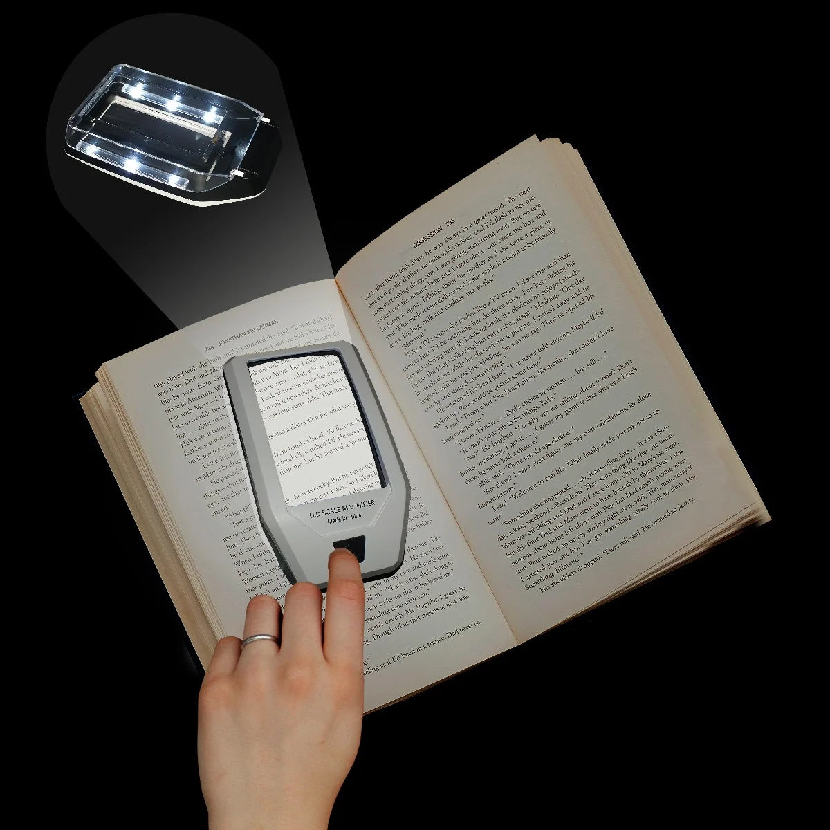 Hand holding a small rectangular illuminated magnifier over an open book on a black background