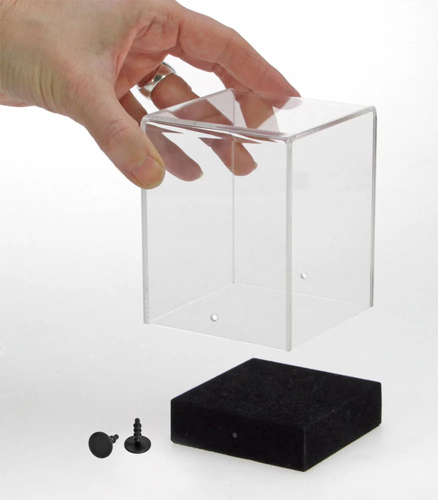 Empty acrylic display case cube being lifted off of the black base by a hand on a white background