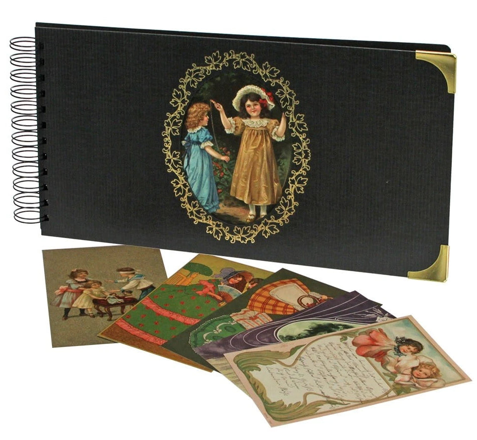 A vintage-style spiral-bound album or photo book with a black textured cover, gold corner protectors, and an oval illustration of two children. Several illustrated cards are fanned out in front on a white background.