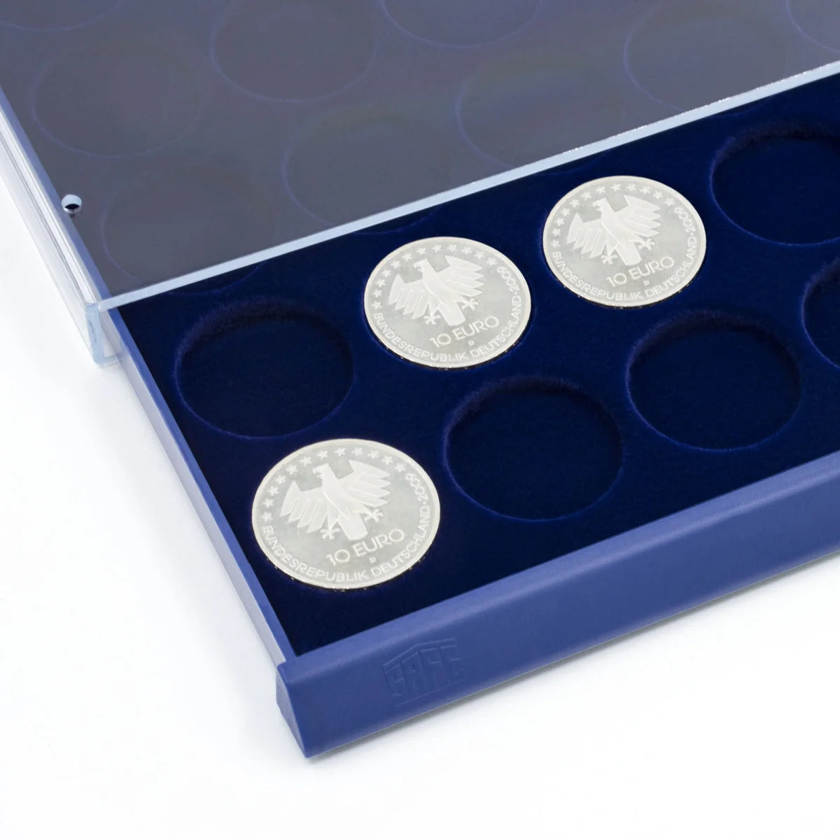 Detail shot of open acrylic stackable drawer unit with a blue velvet tray and circular compartments for coins on a white background