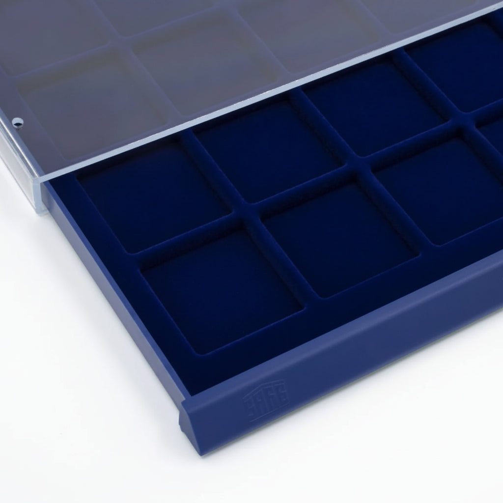 Detail shot of open acrylic stackable drawer unit with a blue velvet tray and square compartments for coins on a white background