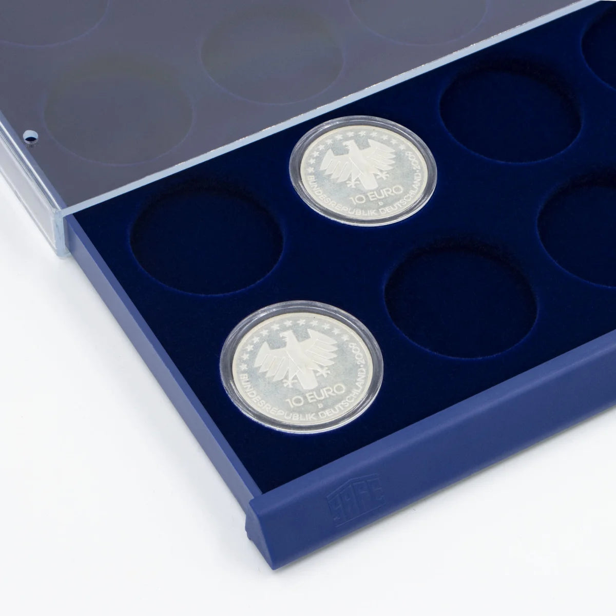 Detail shot of open acrylic stackable drawer unit with a blue velvet tray and circular compartments for coins on a white background