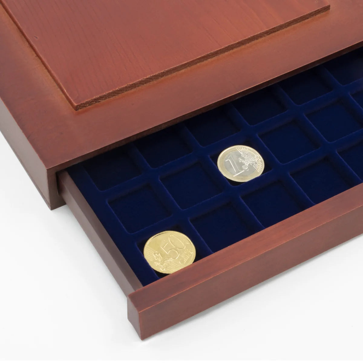 Detail shot of open wooden stackable drawer unit with a blue velvet tray with square compartments holding coins on a white background