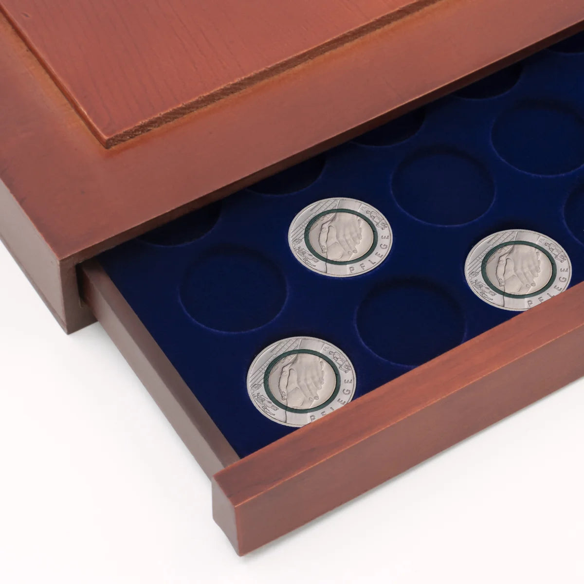 Detail shot of open wooden stackable drawer unit with a blue velvet tray with circular compartments holding coins on a white background