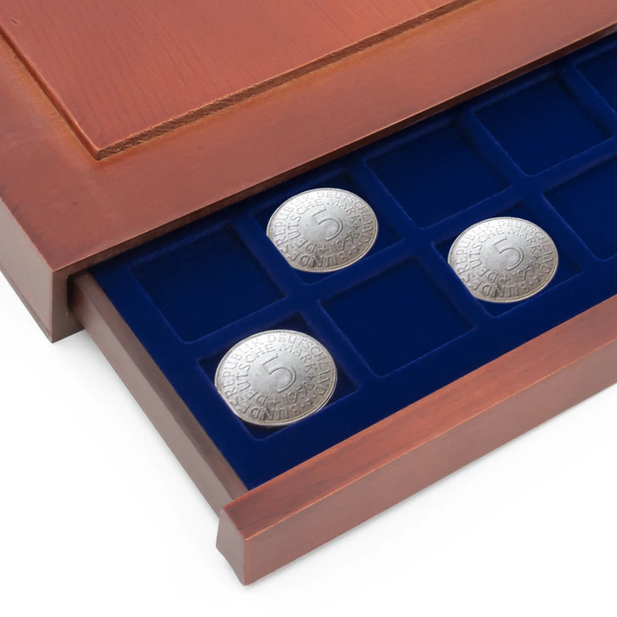 Detail shot of open wooden stackable drawer unit with a blue velvet tray with square compartments holding coins on a white background