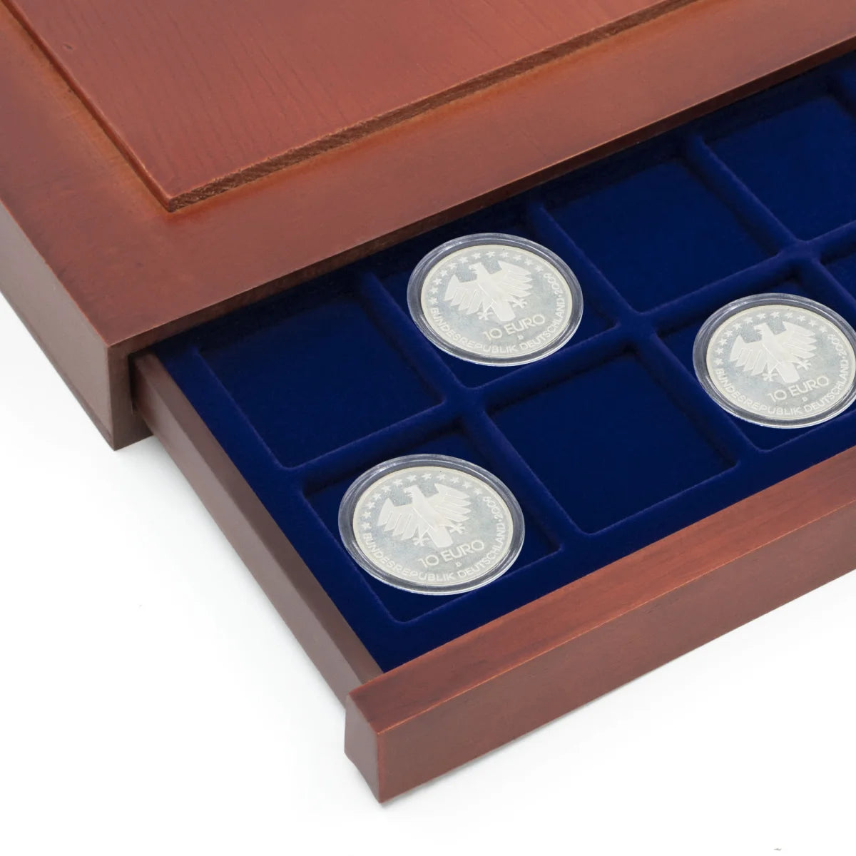 Detail shot of open wooden stackable drawer unit with a blue velvet tray with square compartments holding coins on a white background