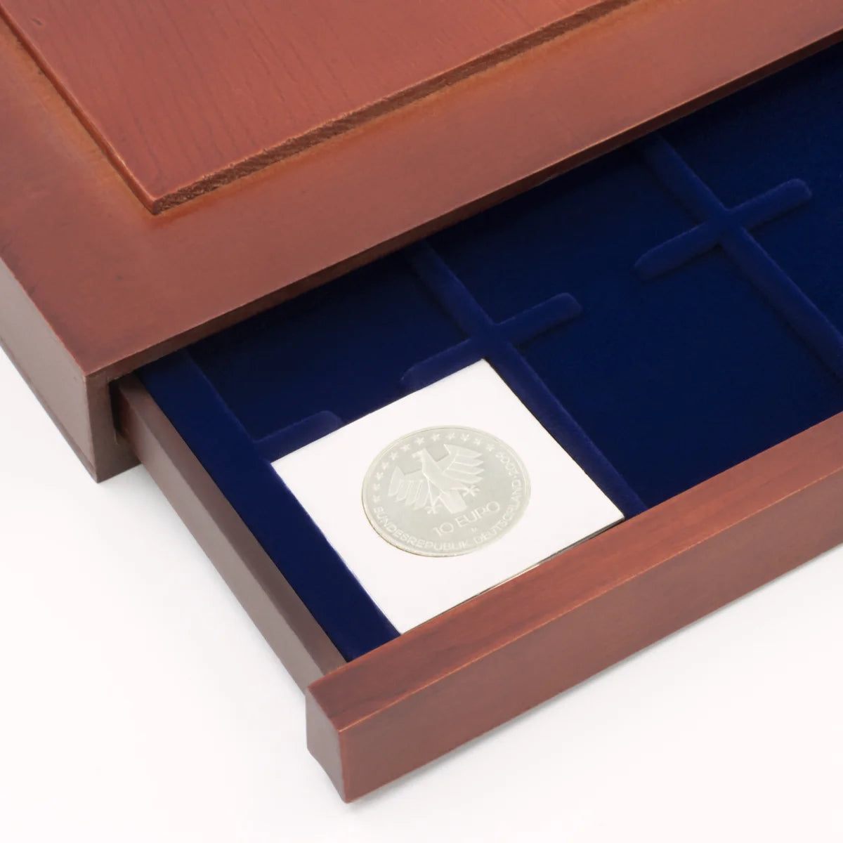 Detail shot of open wooden stackable drawer unit with a blue velvet tray with a self sealing 2x2 coin flip on a white background