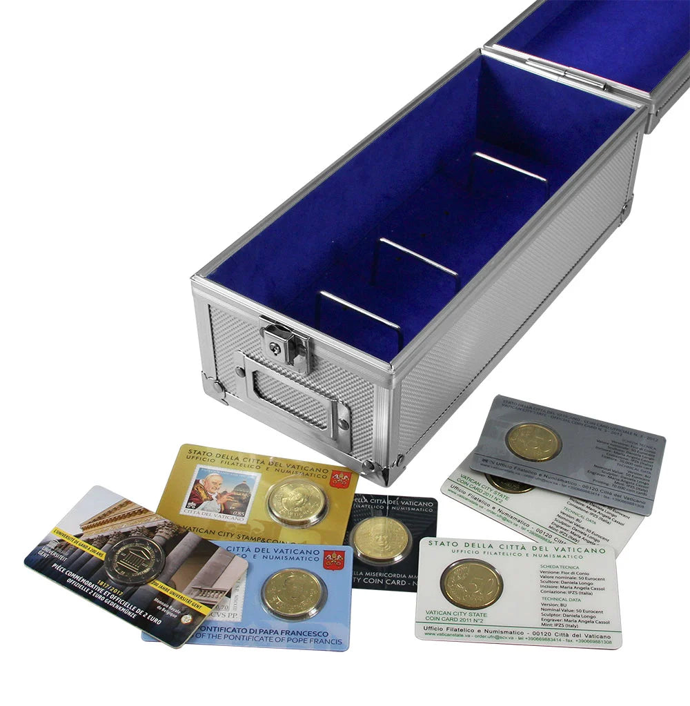 A silver metal coin case with a bright blue velvet interior, shown open with several coins in protective cards and sleeves placed around it on a white background.