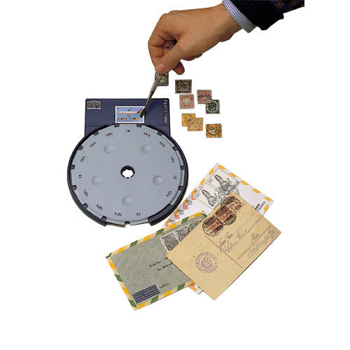 A hand holds a stamp alongside a stamp perf gauge, with several small stamps and vintage envelopes shown on a white background.